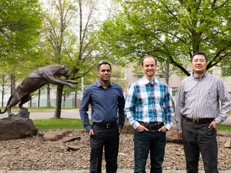 Three men standing by statue of cougar