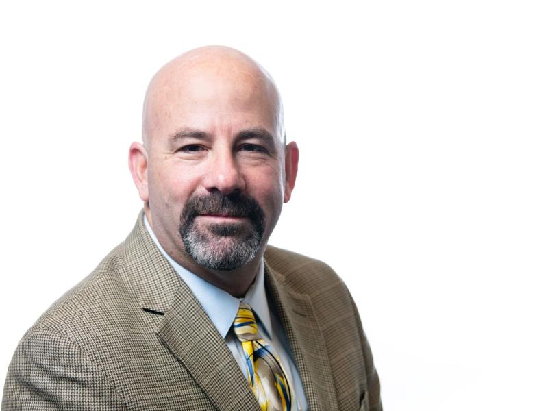 Matthew Paiss, wearing a tan suit jack, a tie, and white shirt.