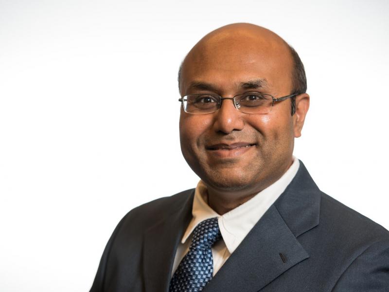 Image of slightly smiling man with glasses in a suit and tie 