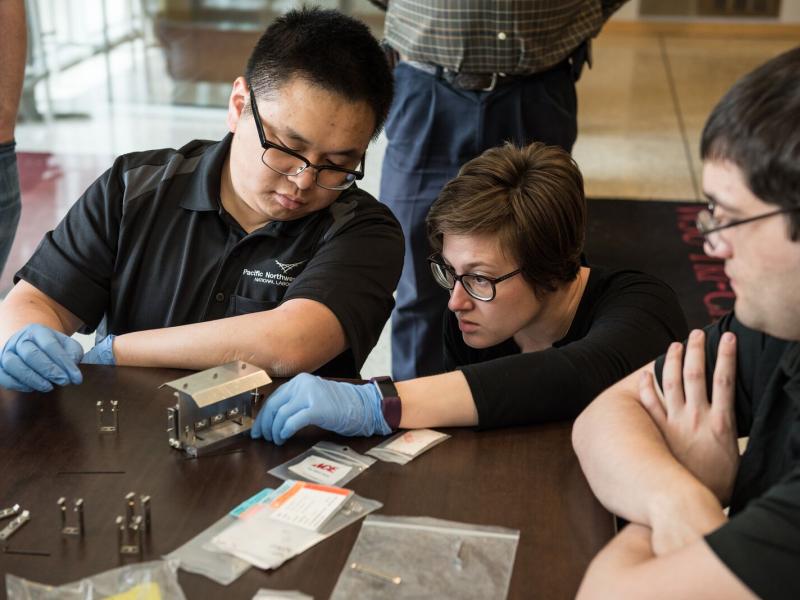 Photo of three students looking at silver device on a table