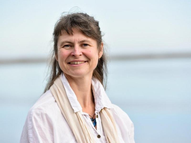 Lady in white shirt with dark hair, water in background