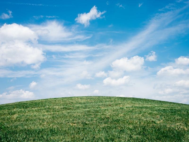 Clouds on a bright blue sky above a grassy hill