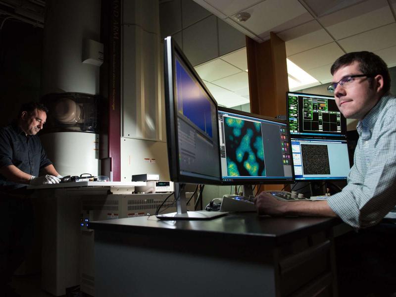 Two men are using a large electron microsope to do science research.