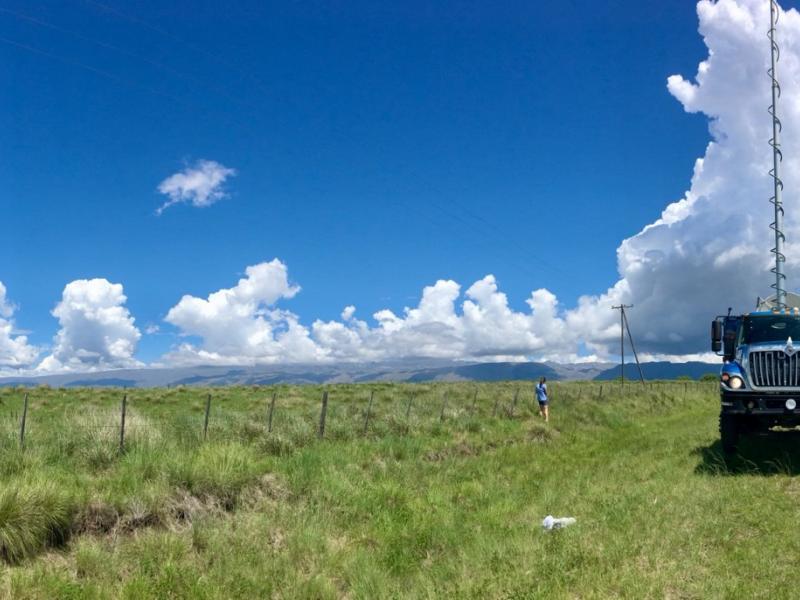 A doppler on wheels mobile weather radar setup on the right side of a photograph with a bright blue sky and green, grassy field