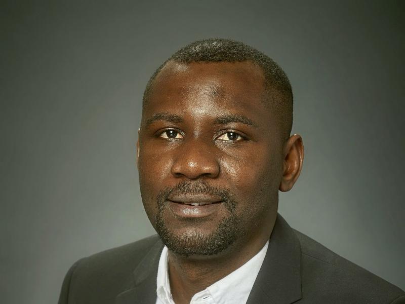 Image of a slightly smiling African man in a white shirt and dark suit