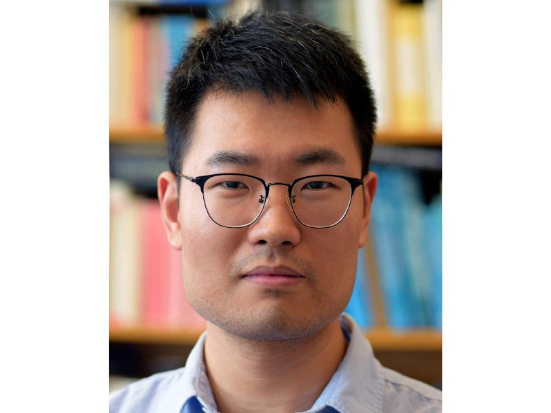 Qingpu Wang wearing glasses in front of colorful books