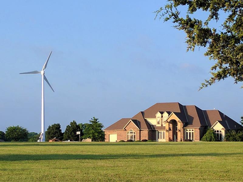 A field with a large house and small wind turbine