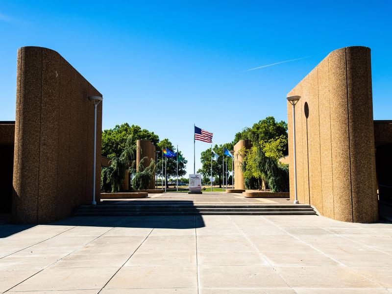 an open plaza with a flag pole flying the American flag in the center, flagged by sand-colored rounded tower buildings