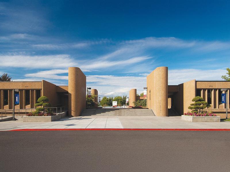 a wide view of a collection of brown cylindrical tower buildings and long glass-fronted towers around a concrete plaza