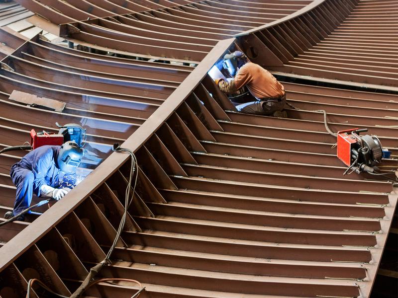 Workers welding pieces onto the frame of a ship.