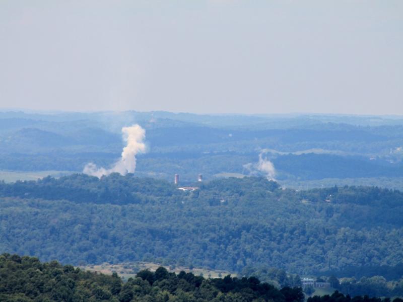 Photograph of smoke coming out of an industrial area surrounded by a forest