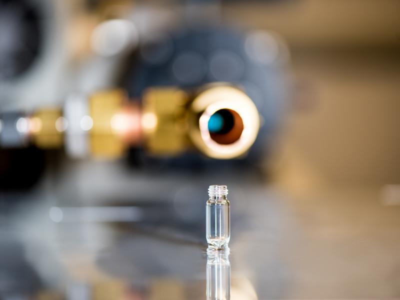 Small vial with a gold laboratory equipment in background.