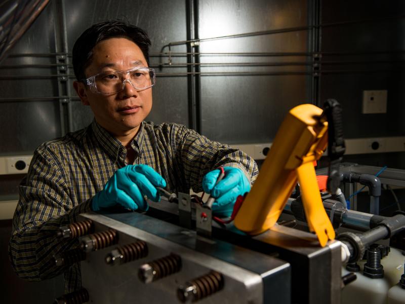 Photo of materials scientist Wei Wang in safety gloves and glasses operating machinery