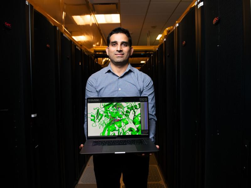 man holding a laptop in an aisle of tall computer servers