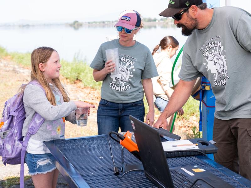 Student holds cup with salmon inside and talks to two STEM ambassadors