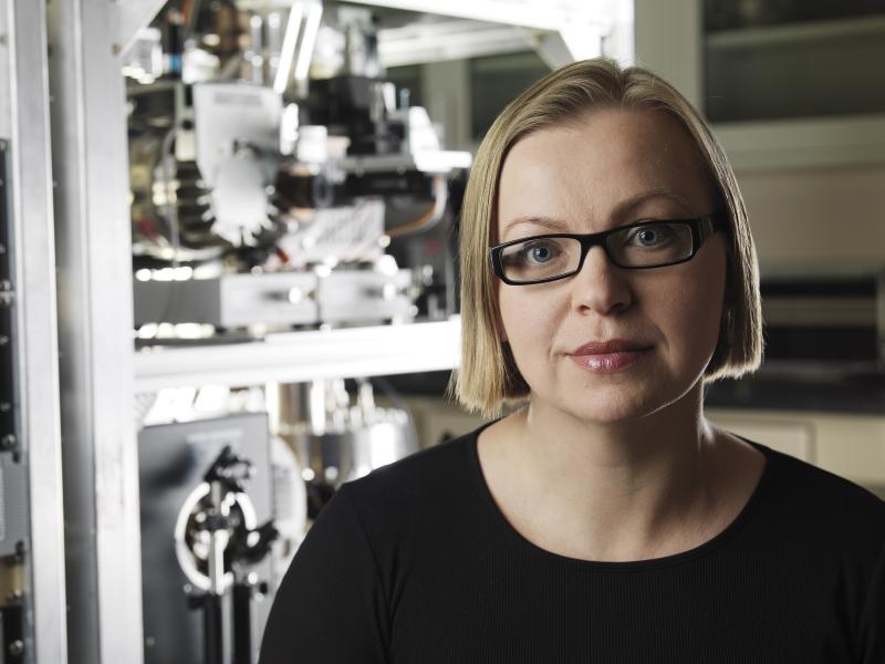 Photograph of a woman wearing glasses in front of scientific equipment