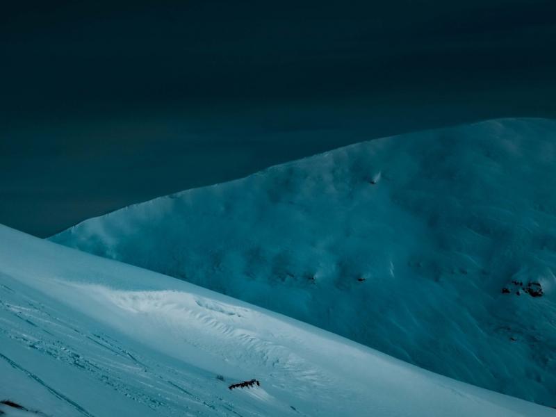 Photograph of Arctic mountains covered in snow bathed an a dark blue light.