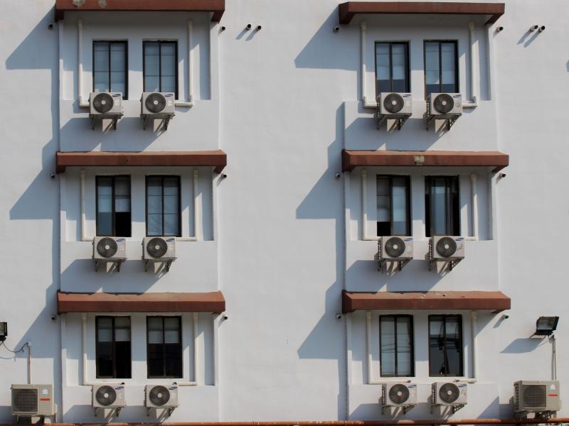 Air conditioning units sit outside a hotel building face, one attached to each window.