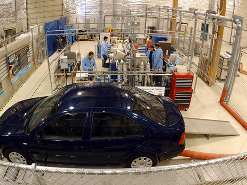 Photo of researchers working in a small facility behind a parked, blue car.