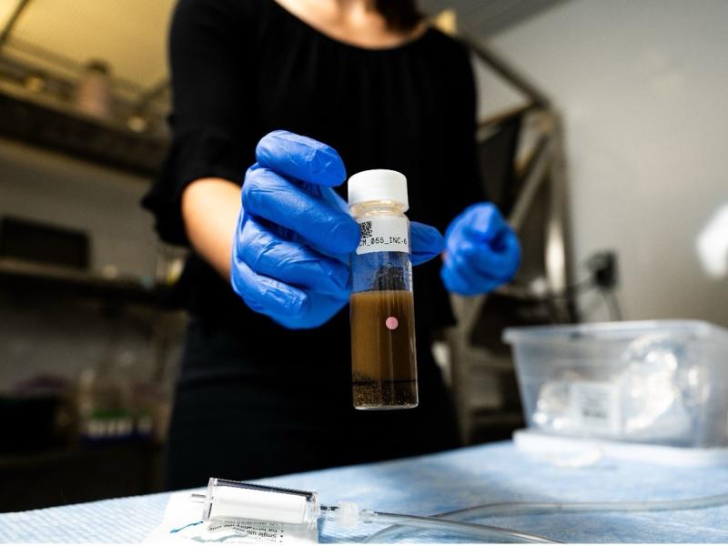 a researcher holds a vial of river sediment and water taken to sample respiration