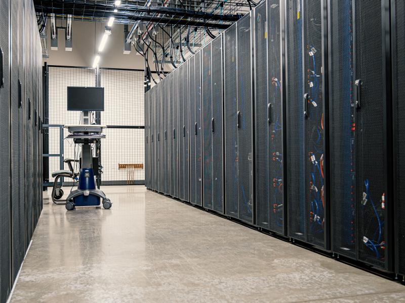 Image shows an aisle of black mesh cabinets holding data center servers.
