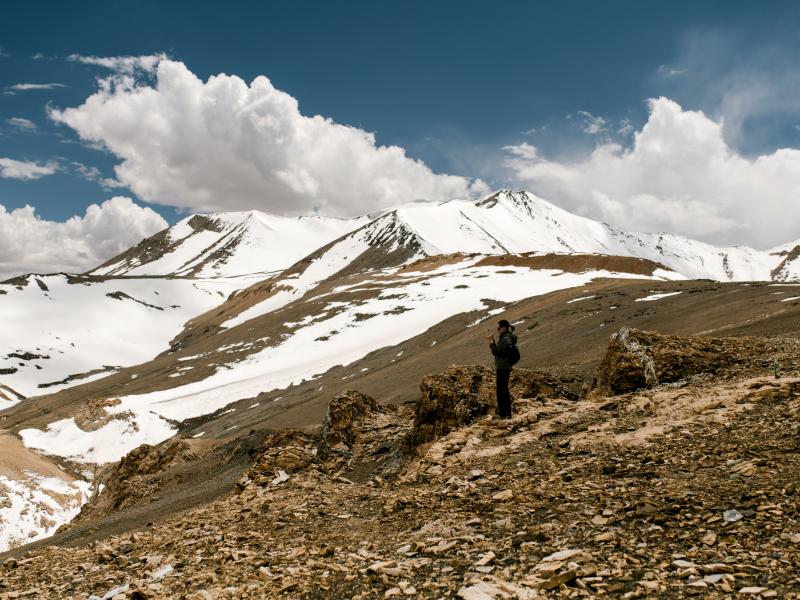 Photo of a person standing on top of mountain. There are scattered patches of snow behind them.