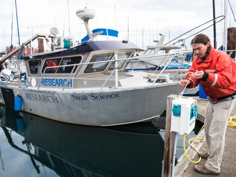 Photo of a researcher standing in front of a boat at a dock.