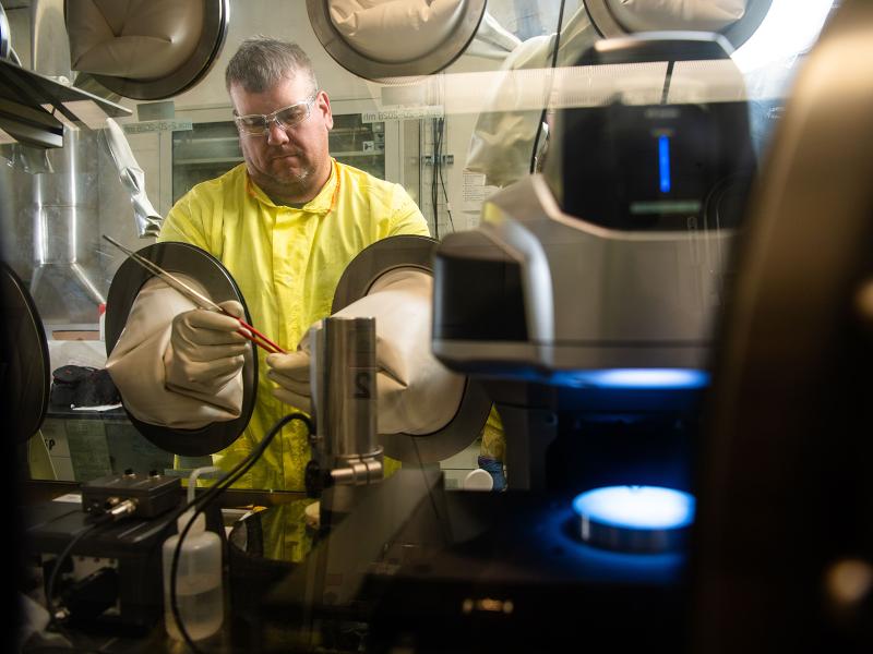 a researcher in protective gear works in an isolated glove box
