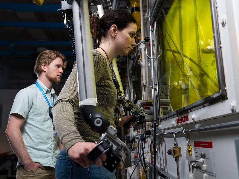 researchers in a darkened lab look into a protected box through a yellow-tinged window