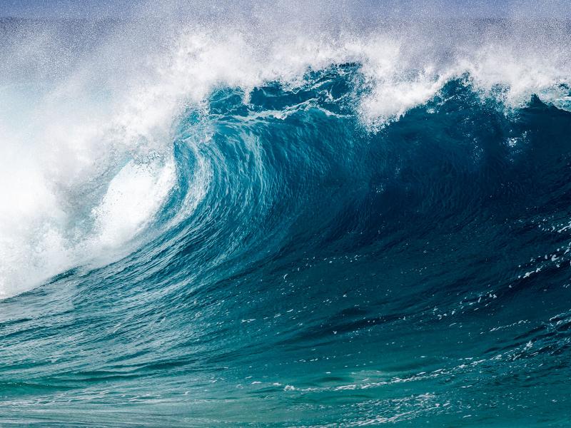 An ocean wave crests, releasing ocean mist just before crashing down. 