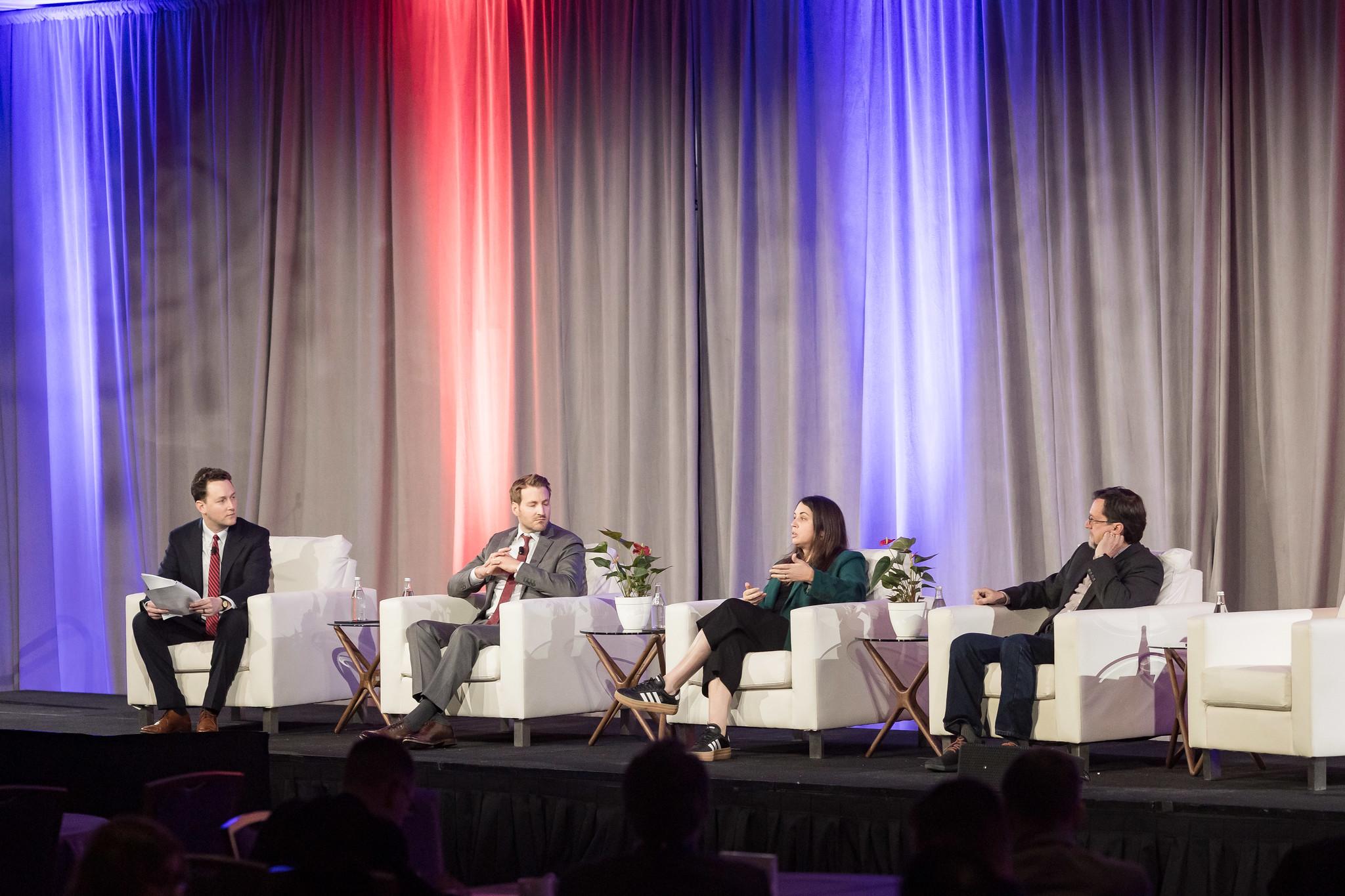 John VerWey and 3 other people sitting in chairs for panel discussion on a stage