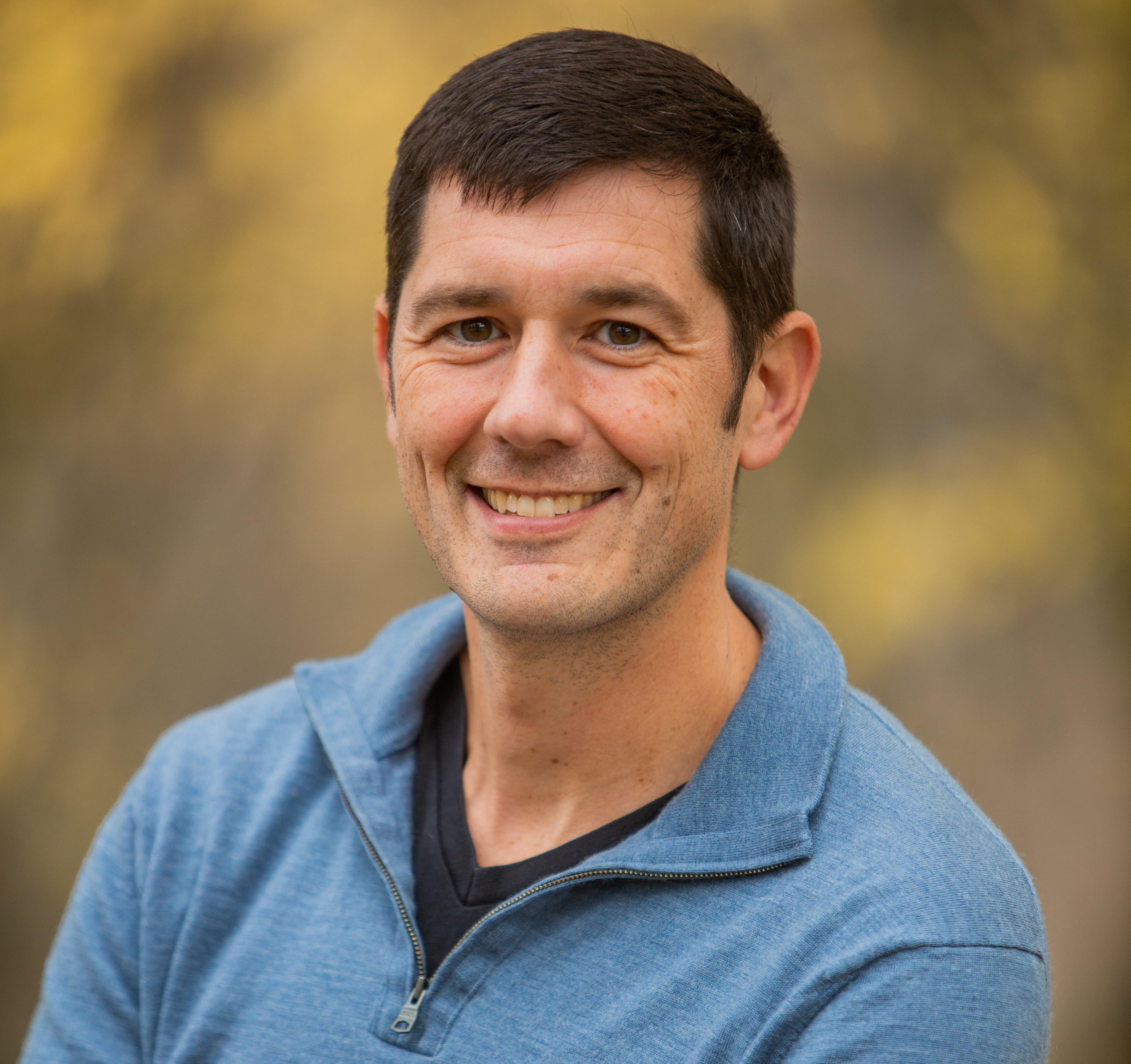 photo of a man with brown hair in a blue sweater. 