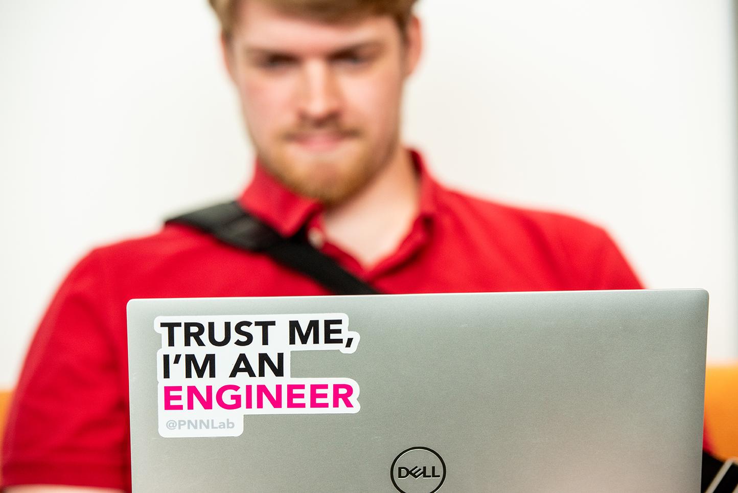 Man holding a laptop computer with a sticker on it