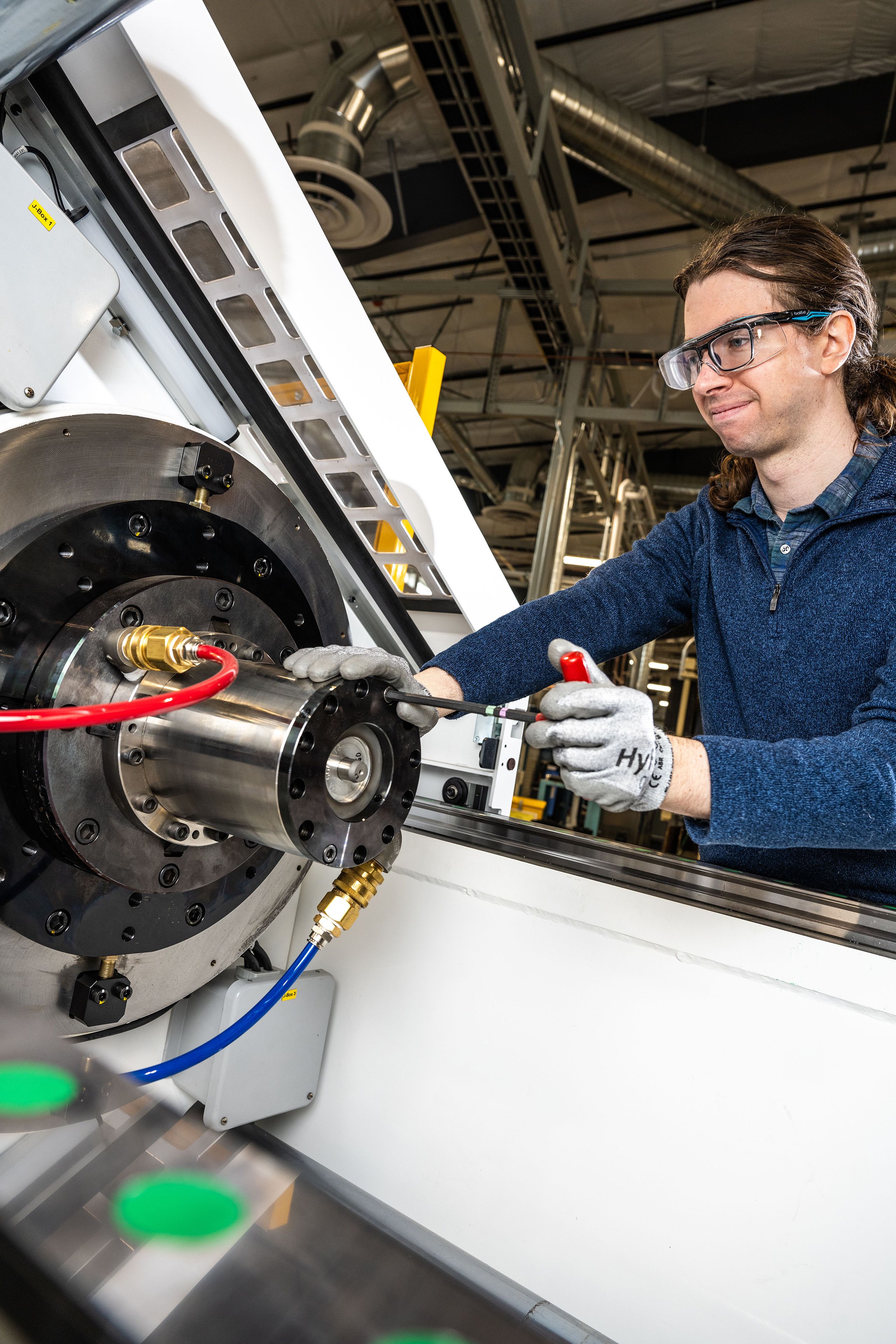 A researcher in safety glasses and gloves uses a tool to make adjustments to a large cylindrical device