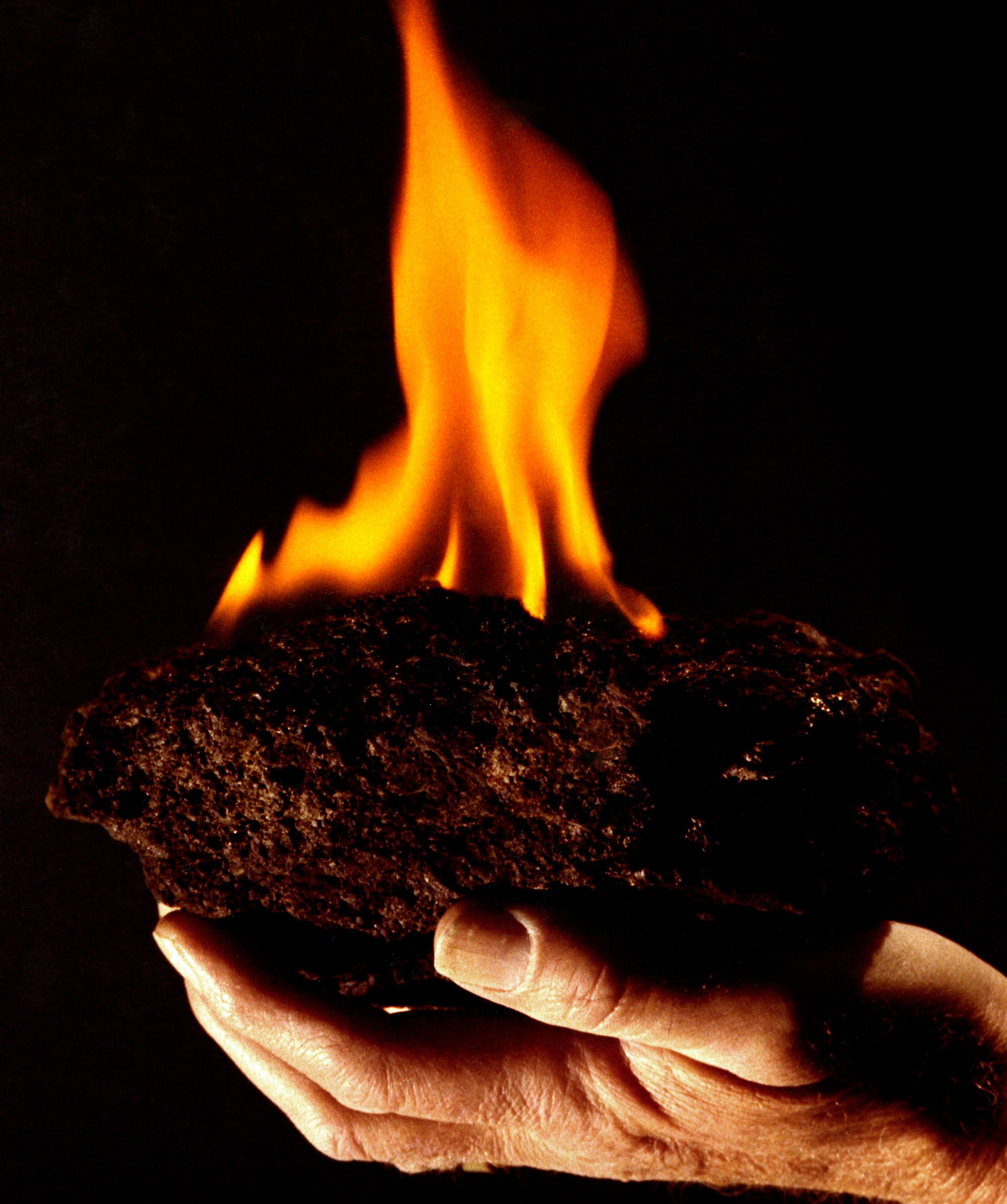 Tight-focus on a hand holding a flaming piece of dark material