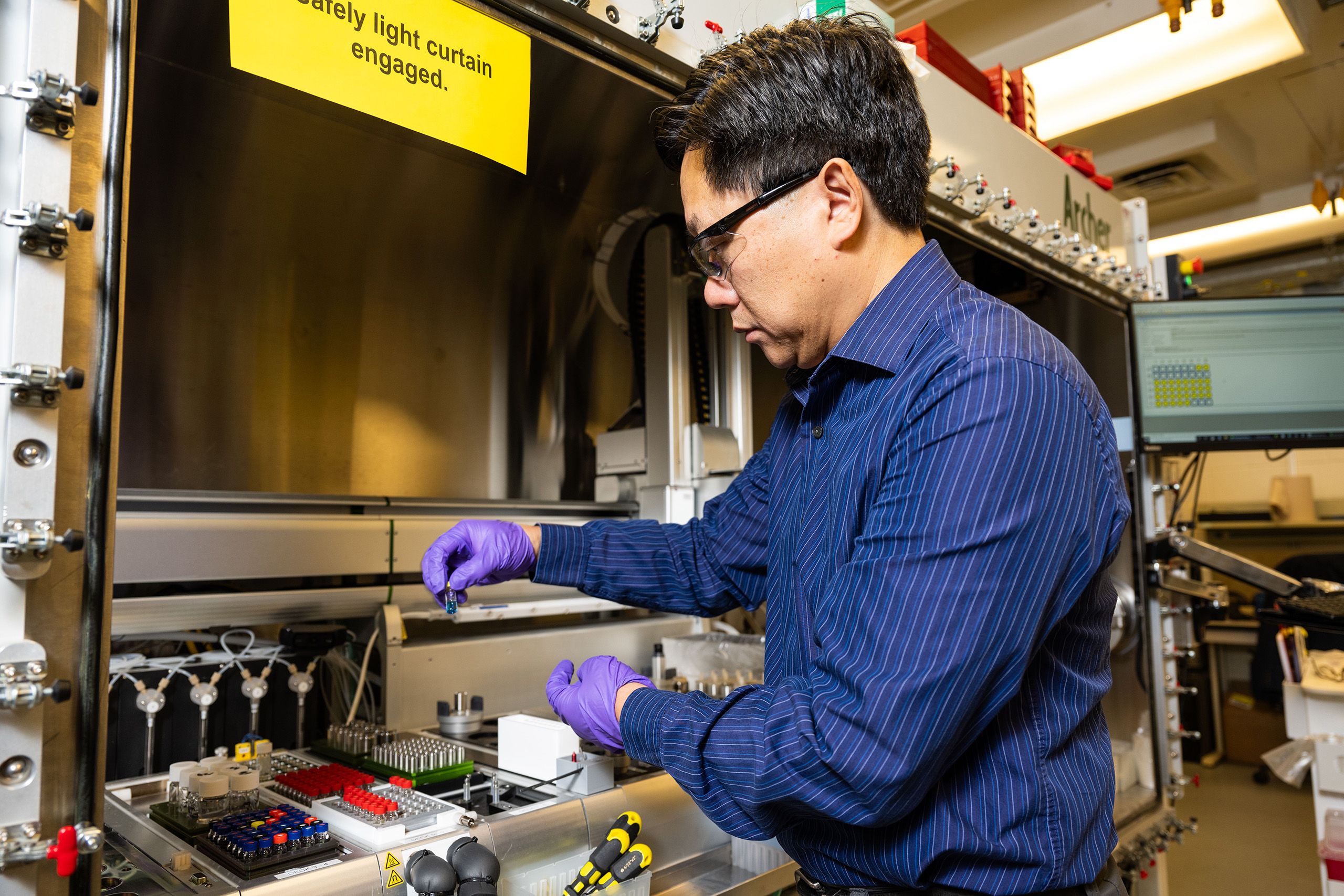 a researcher wearing safety glasses and gloves examines a piece of lab equipment