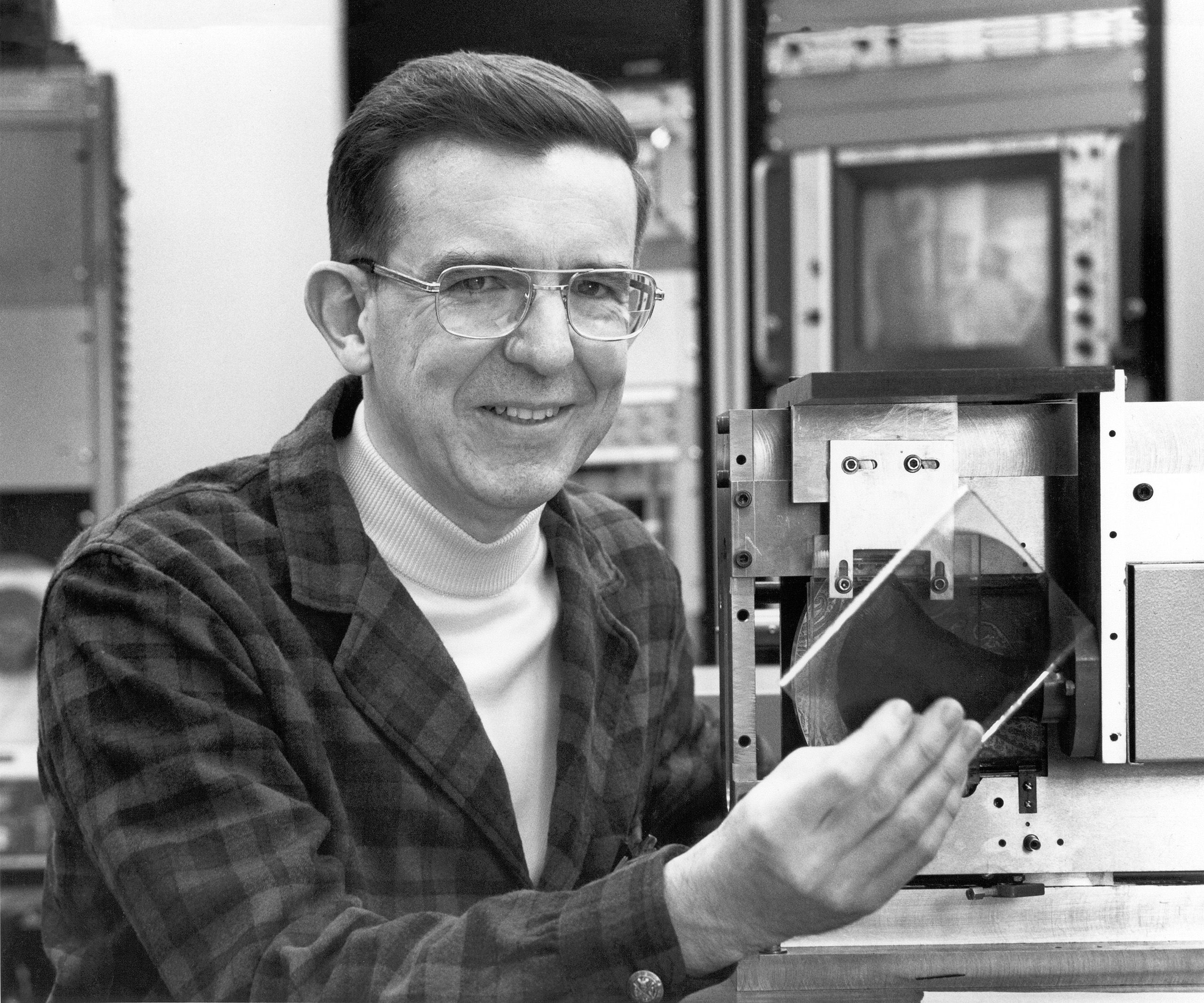 a black and white historical photo of a researcher in glasses holding a piece of transparent material