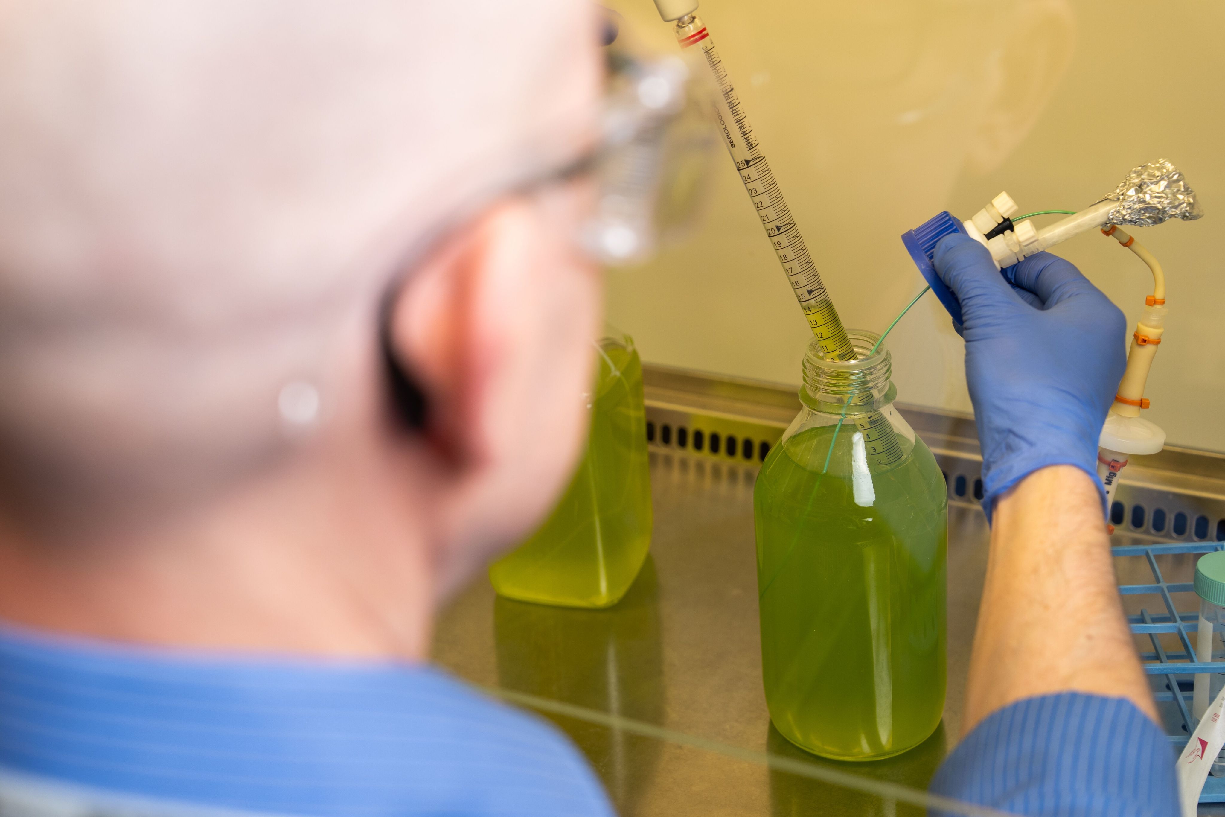 a researcher wearing safety gloves pipettes bright green liquid from a glass bottle